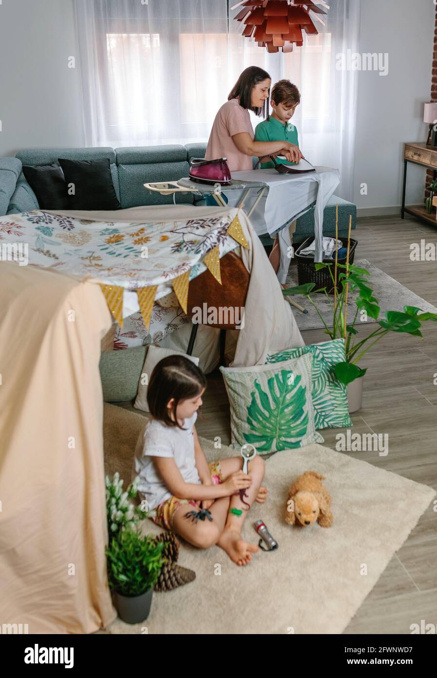 Madre insegnando il suo figlio adolescente a ferro mentre sua figlia gioca in campeggio a casa Foto Stock