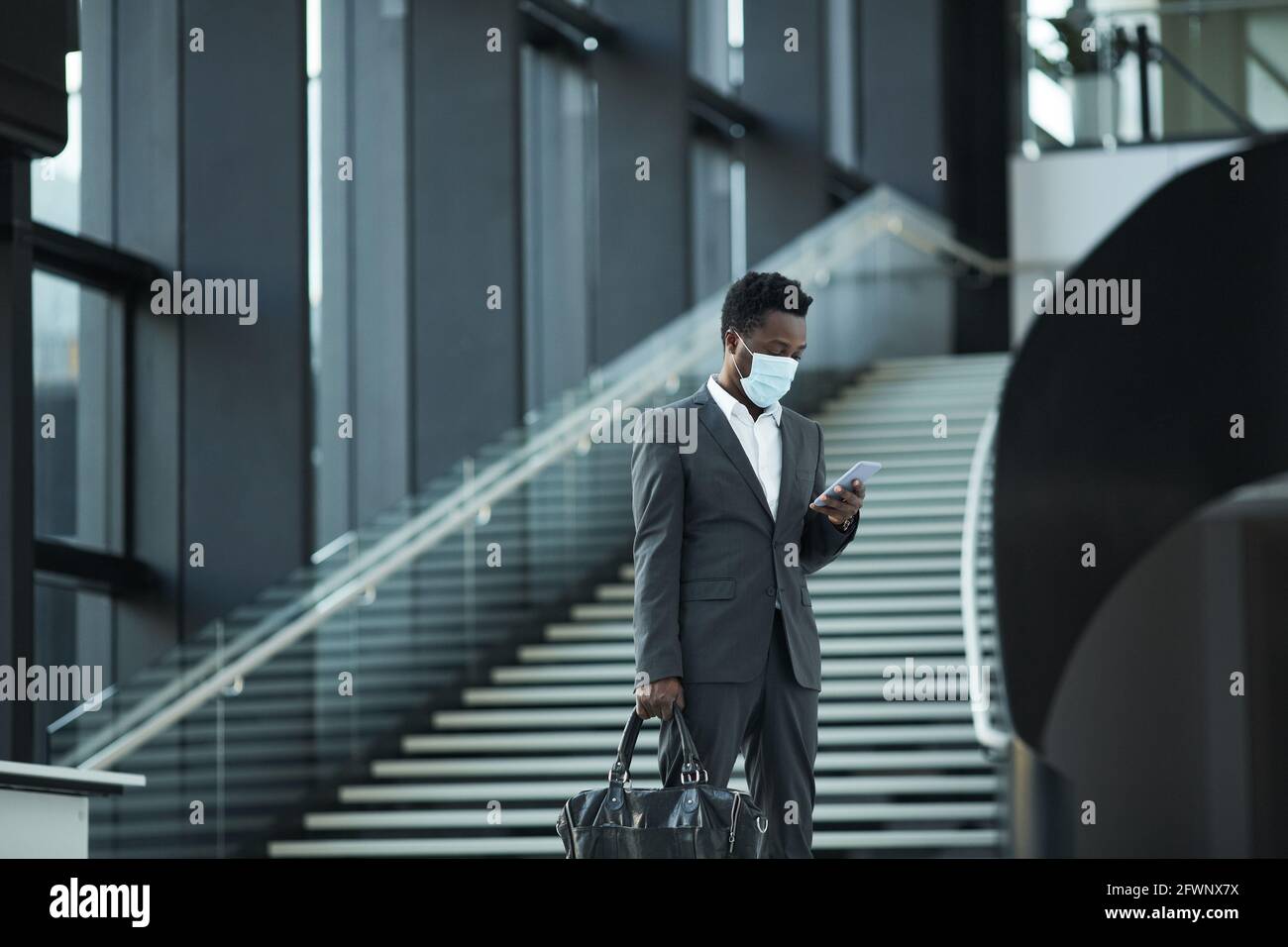 Ritratto grandangolare di successo afro-americano uomo d'affari indossare maschera mentre si cammina verso la fotocamera in ufficio edificio, copia spazio Foto Stock