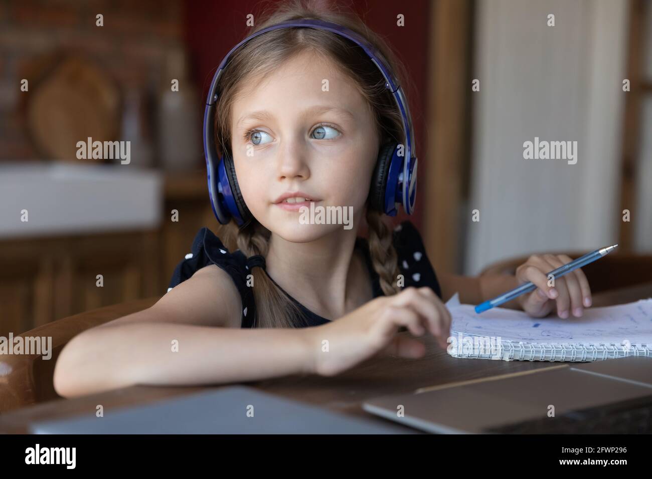 Studentessa pensiva indossando le cuffie che fanno i compiti della scuola a casa Foto Stock