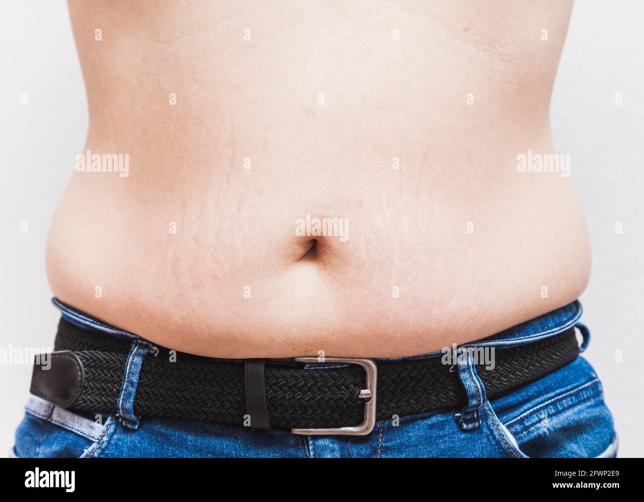 Il ventre e l'ombelico di un uomo grasso irriconoscibile che indossa jeans blu e una cintura nera Foto Stock
