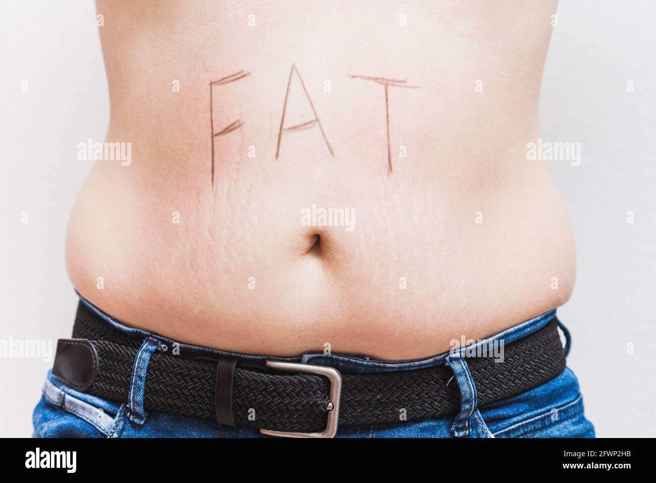 La parola 'grasso' scritta sul ventre di un uomo grasso irriconoscibile. L'uomo è vestito di jeans e indossa una cintura nera. Foto Stock