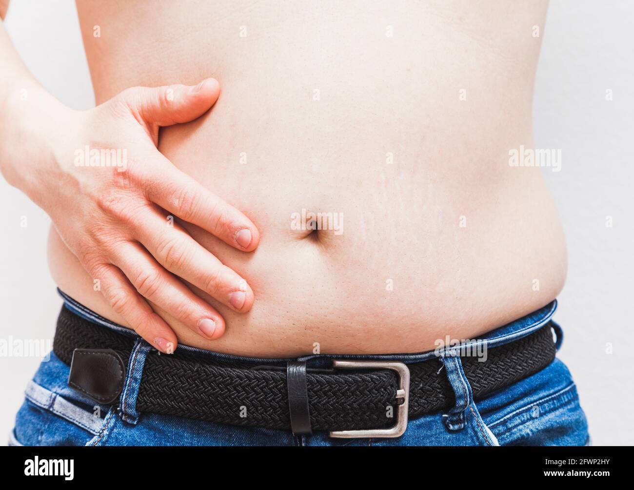 Un uomo grasso irriconoscibile tocca il ventre con il palmo della mano. L'uomo indossa jeans blu e un essere nero Foto Stock