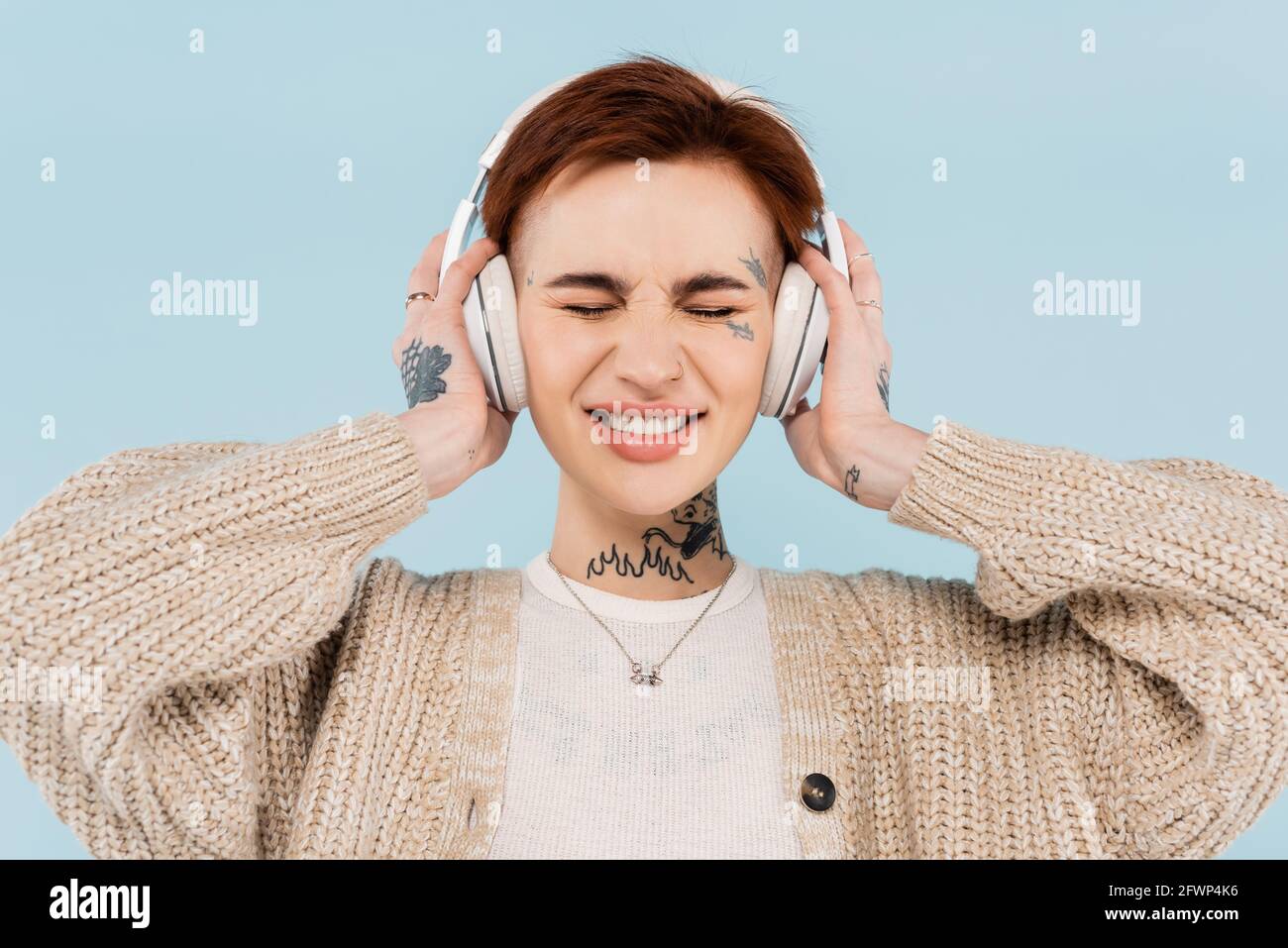 donna sorridente con tatuaggi e occhi chiusi in cuffie wireless isolato su blu Foto Stock
