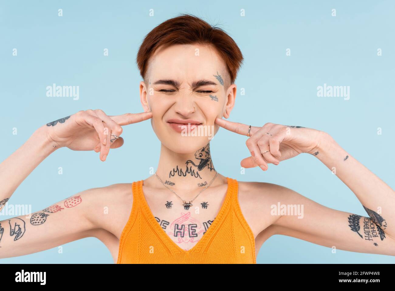 donna con tatuaggi e canotta in maglia arancione che punta guance isolate su blu Foto Stock