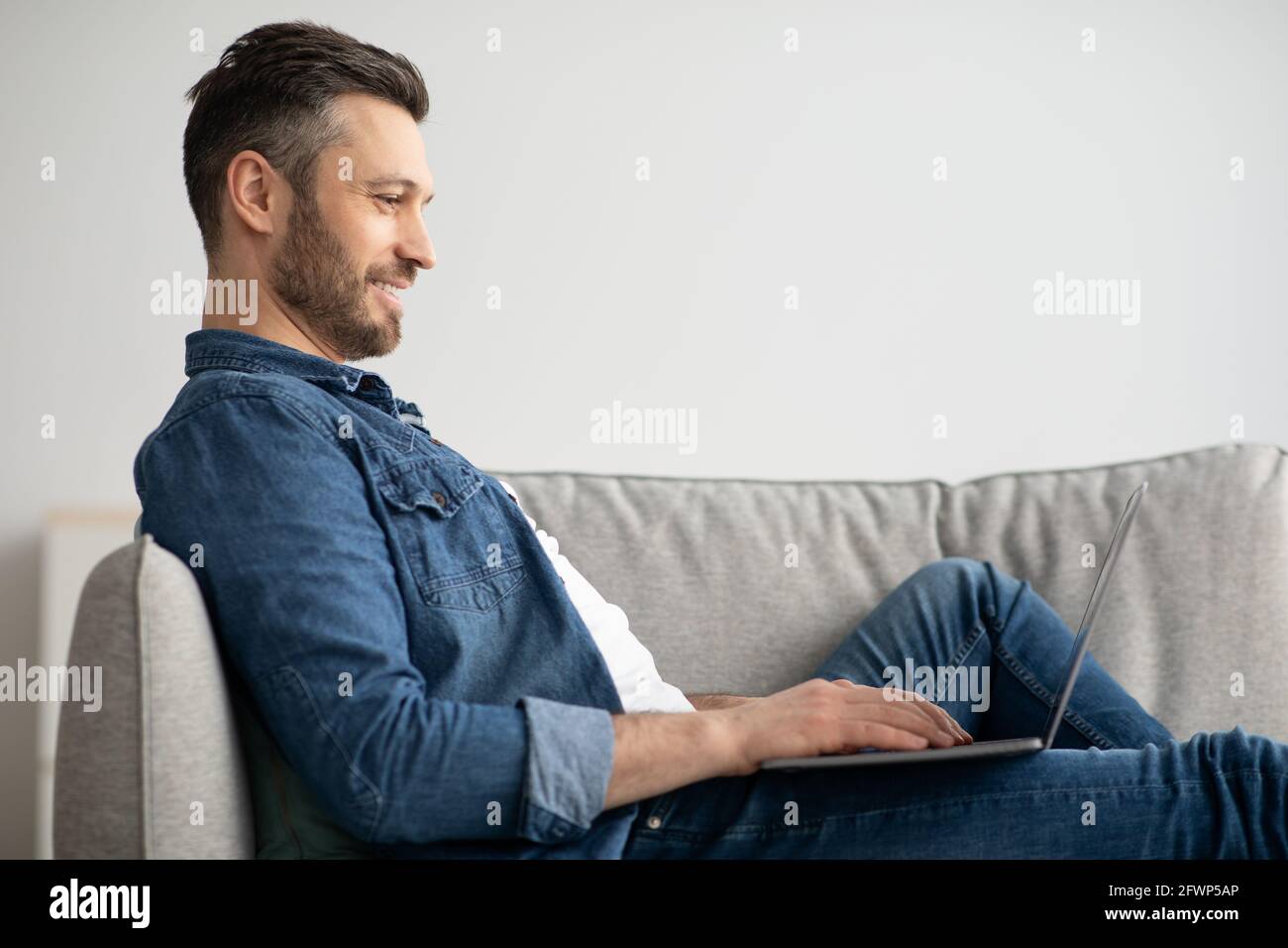 Uomo sorridente che usa il laptop, avendo un lavoro part-time a casa Foto Stock