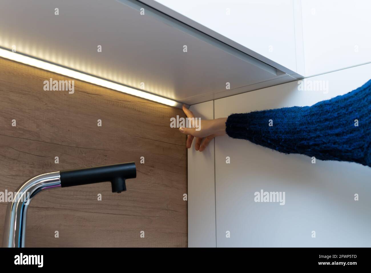La mano femmina include una striscia LED per l'illuminazione sul superficie dell'armadio sul set da cucina Foto Stock
