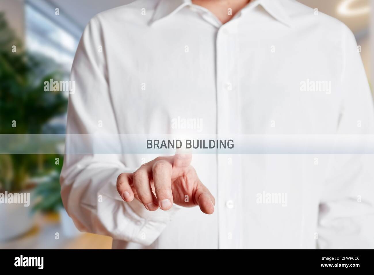 La mano dell'uomo d'affari preme il pulsante di costruzione del marchio su un touch screen virtuale. Branding, marketing e concetto di pubblicità. Foto Stock