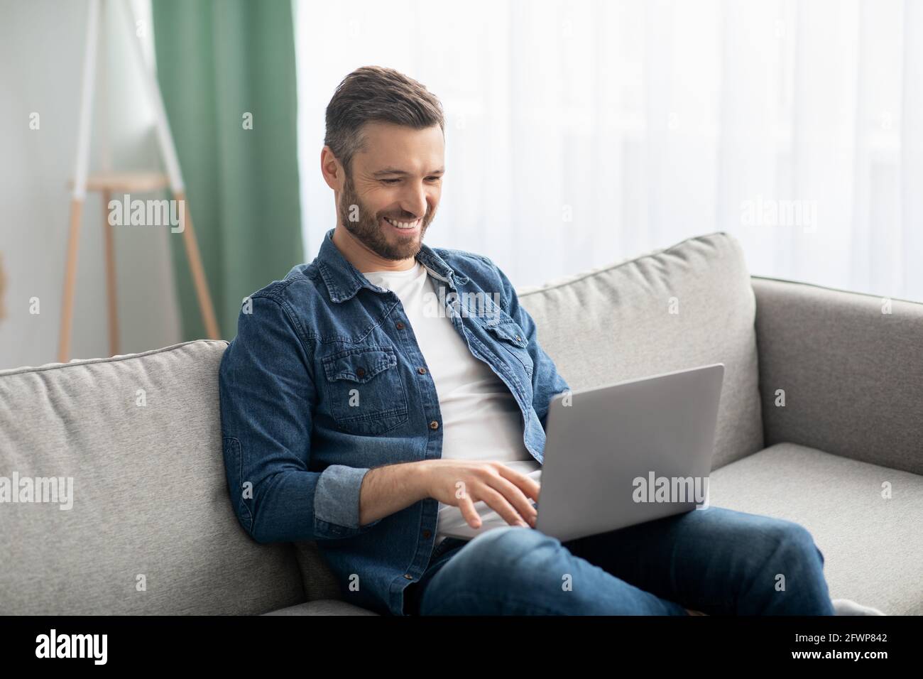 Sorridente uomo di mezza età seduto sul divano, utilizzando un computer portatile Foto Stock