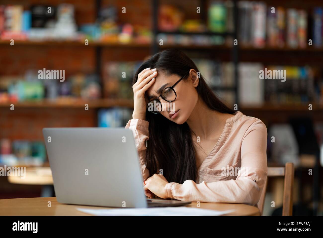 Deluso araba signora usando il laptop e avendo problemi, lavorando al computer a distanza in caffetteria, che soffre di mal di testa Foto Stock