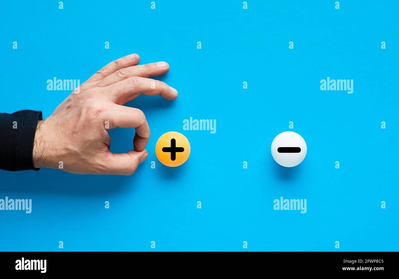 La positività supererà la negatività o i pro scarteranno il concetto di cons. La mano maschile sta per lanciare la palla con il segno più e sparare il meno. Foto Stock