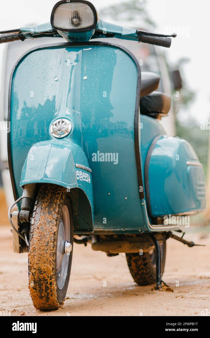 Vespa Scooter vista ravvicinata anteriore, parcheggiata in una strada fangosa in una giornata piovosa. Moto classica vintage Sky Blue. Foto Stock
