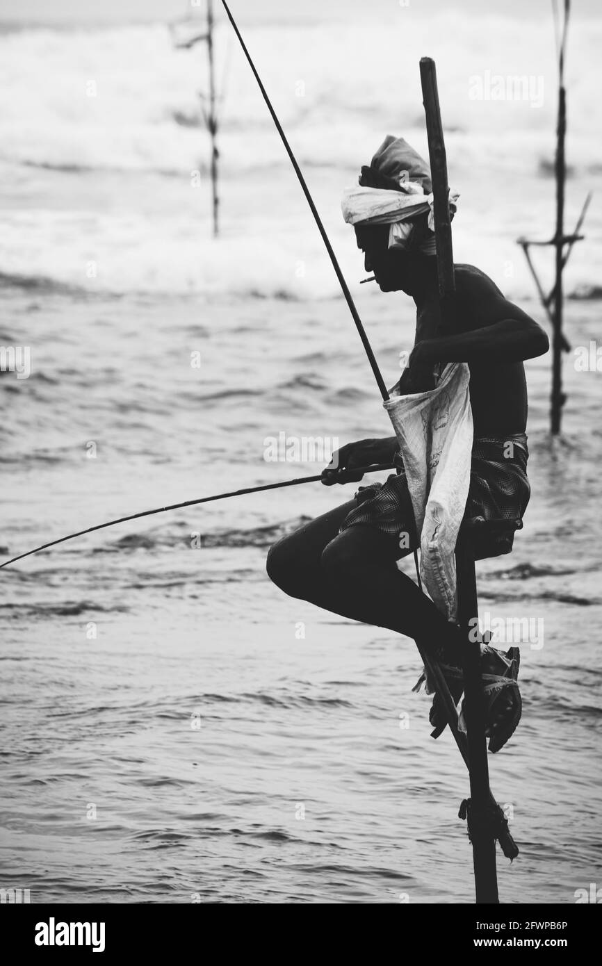 Mirissa, Sri Lanka - 07 26 2020: Silhouette di pescatori tradizionali, canna da pesca, e una borsa per la raccolta del pesce, seduto su una croce bastone sopra la Foto Stock