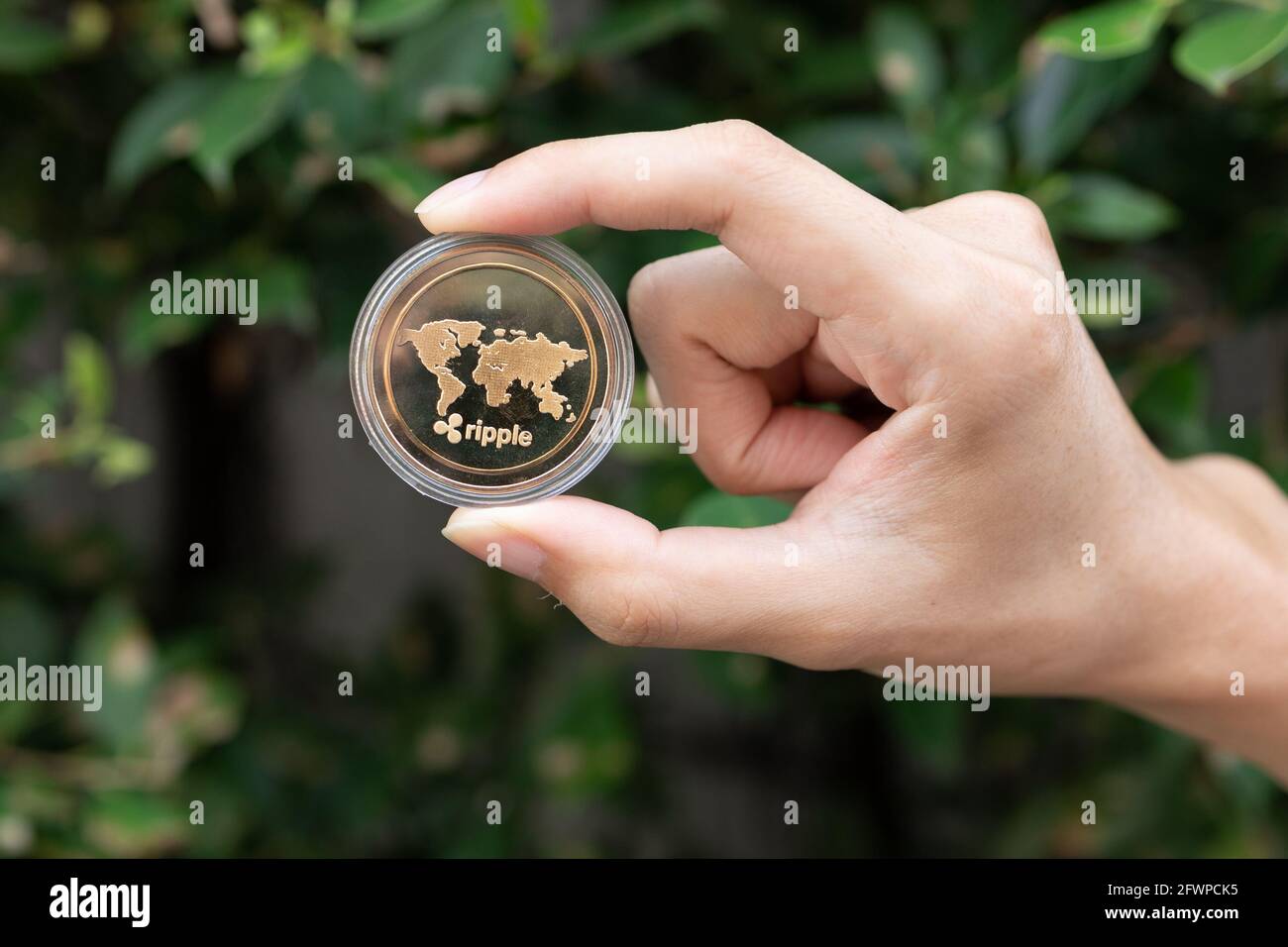 Giovane che tiene in mano la moneta di XRP Ripple con il verde Bush in background - Cryptocurrency e concetto di asset digitale Foto Stock