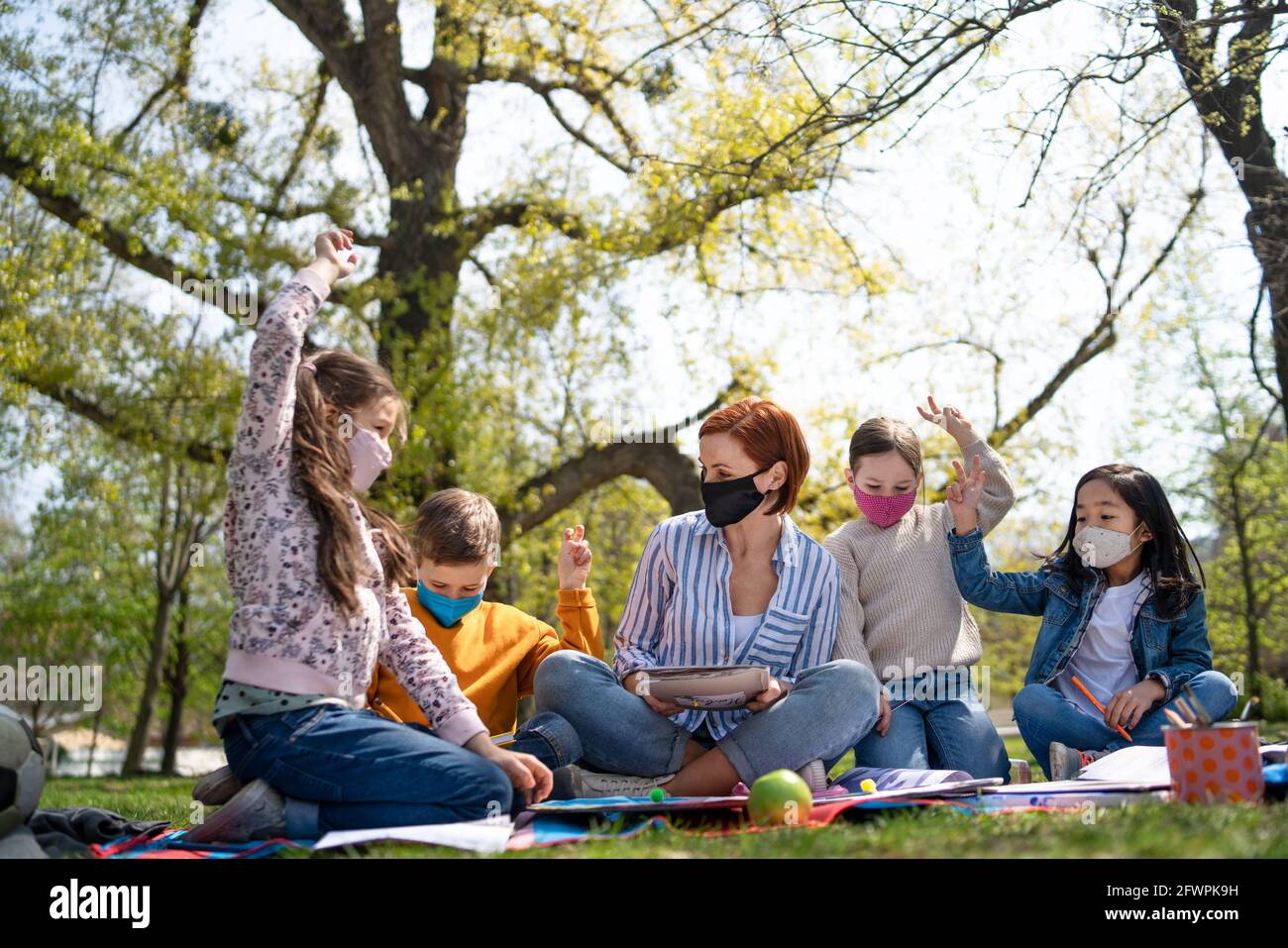 Insegnante con bambini piccoli seduti all'aperto nel parco cittadino, formazione di gruppo e concetto di coronavirus. Foto Stock