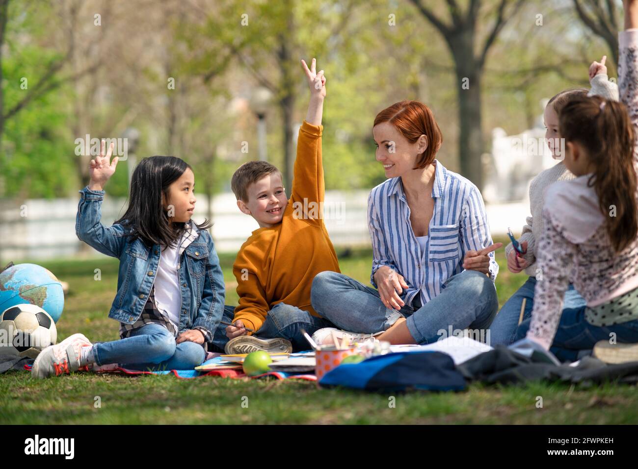 Insegnante con bambini piccoli seduti all'aperto nel parco cittadino, apprendimento concetto di educazione di gruppo. Foto Stock