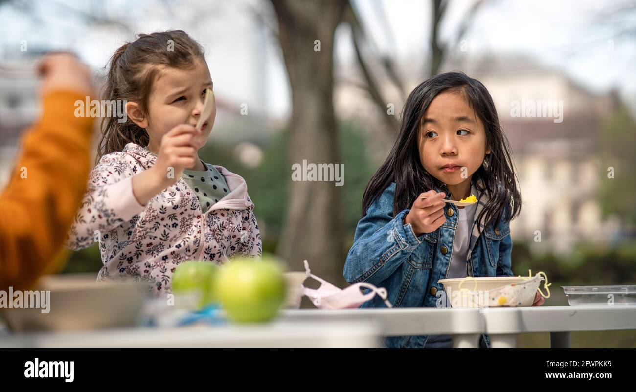 I bambini piccoli mangiano il pranzo all'aperto nel parco cittadino, imparano l'educazione di gruppo e il concetto di coronavirus. Foto Stock