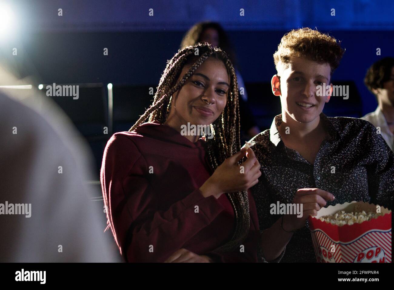Giovane coppia che mangia popcorn mentre guardi un film al cinema, guardando la macchina fotografica. Foto Stock