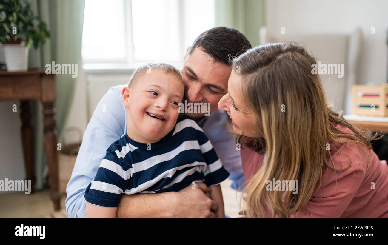 Ragazzo allegro sindrome giù con i genitori all'interno a casa abbracciando. Foto Stock