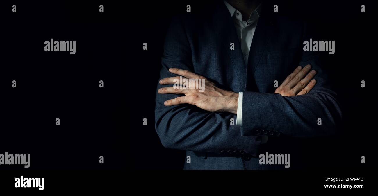 uomo d'affari in tuta con braccia incrociate in piedi su sfondo nero scuro. copia spazio Foto Stock
