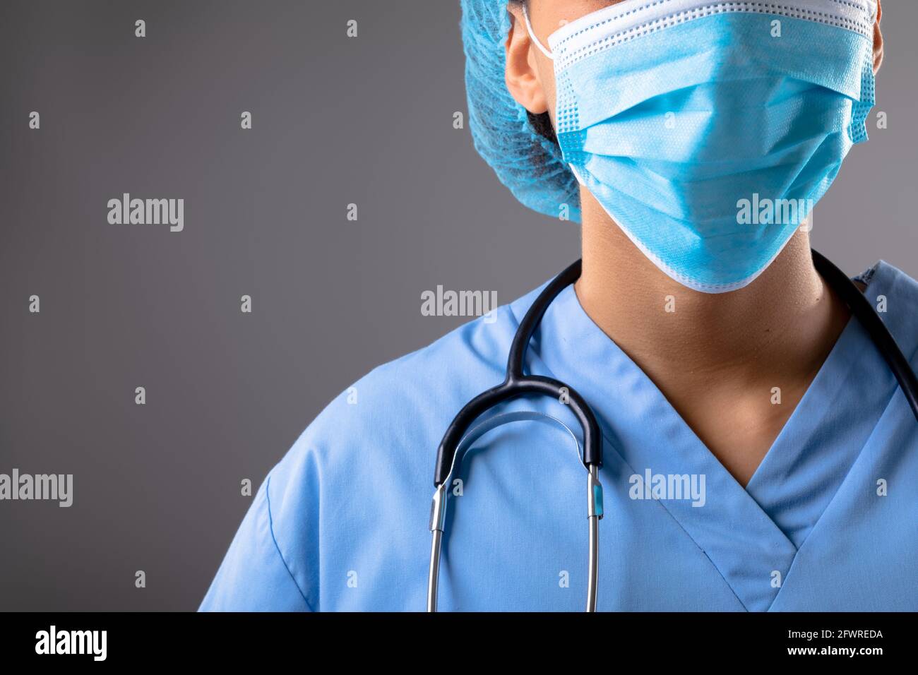 Sezione centrale del chirurgo femminile che indossa la maschera facciale contro il grigio sfondo Foto Stock