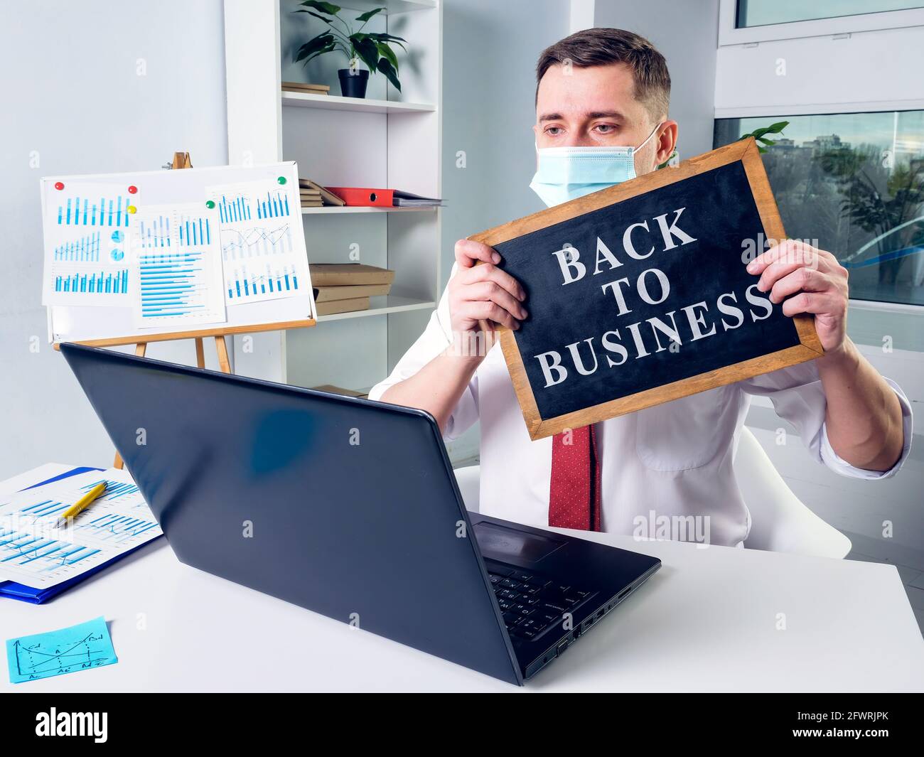 Un uomo d'affari in una maschera mostra un segno indietro al commercio durante la comunicazione in linea. Foto Stock