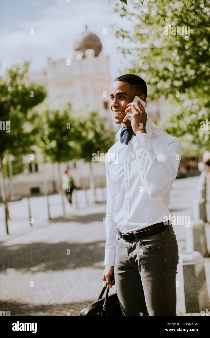 Bel giovane uomo d'affari afro-americano che usa un telefono cellulare mentre attesa per un taxi su una strada Foto Stock