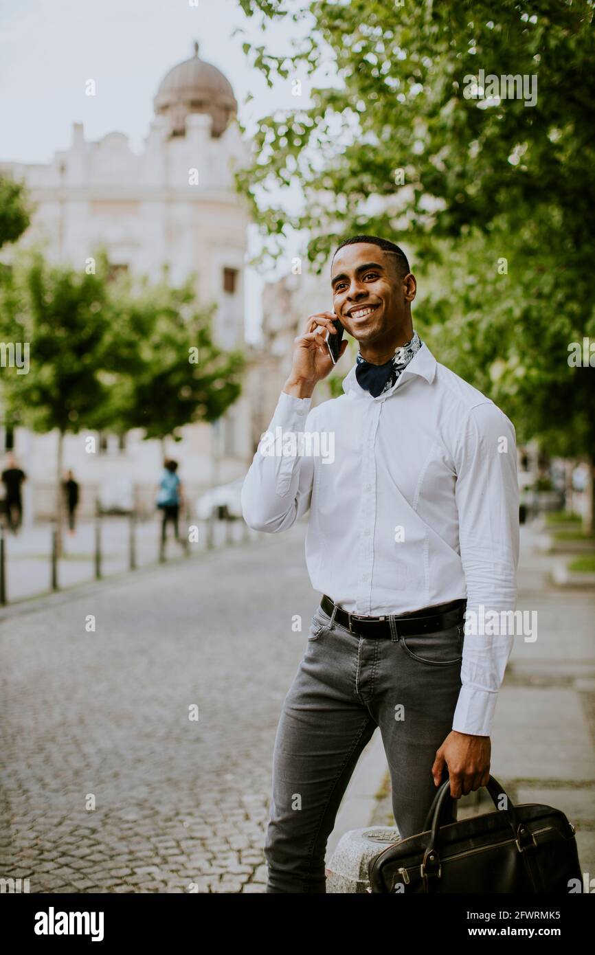 Bel giovane uomo d'affari afro-americano che usa un telefono cellulare mentre attesa di un taxi in attesa di un taxi su una strada Foto Stock