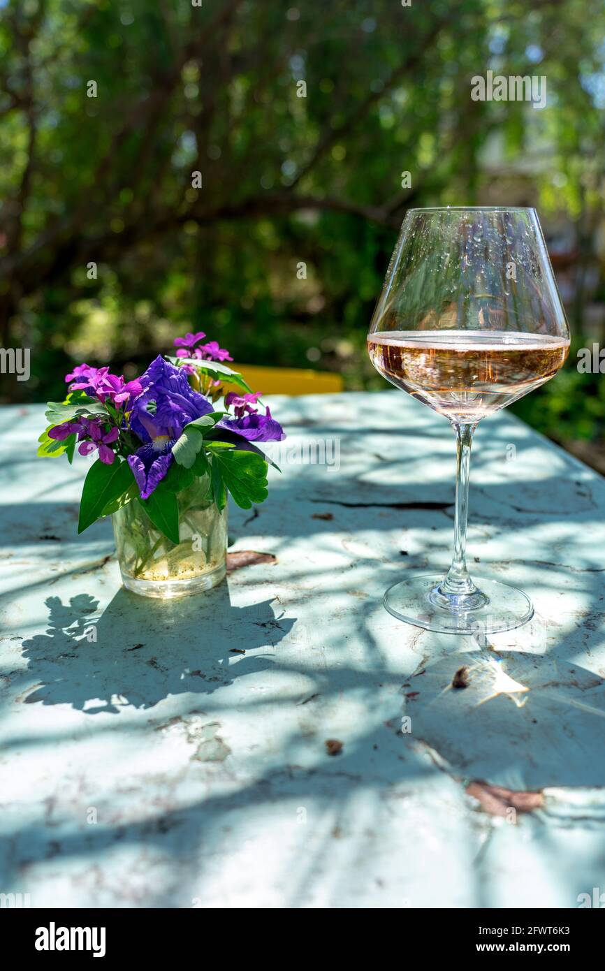 Vintage tavolo esterno in giardino con un bicchiere di vino rosato e fiori . Foto Stock