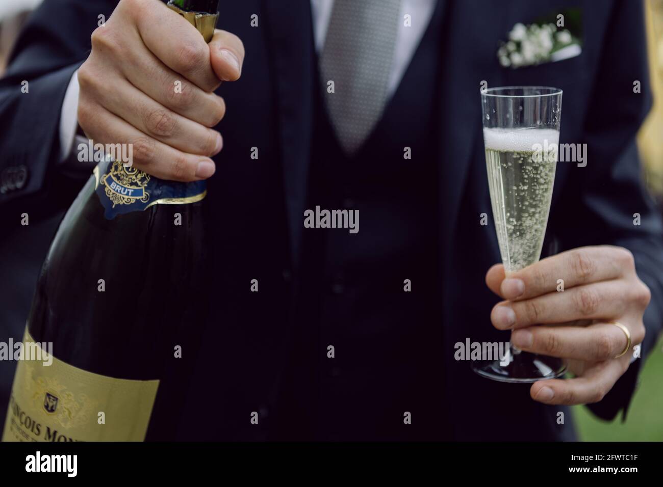 Uomo elegante con una bevanda e una grande bottiglia di vino, brinda con prosecco di vino frizzante all'aperto, all'aperto Foto Stock