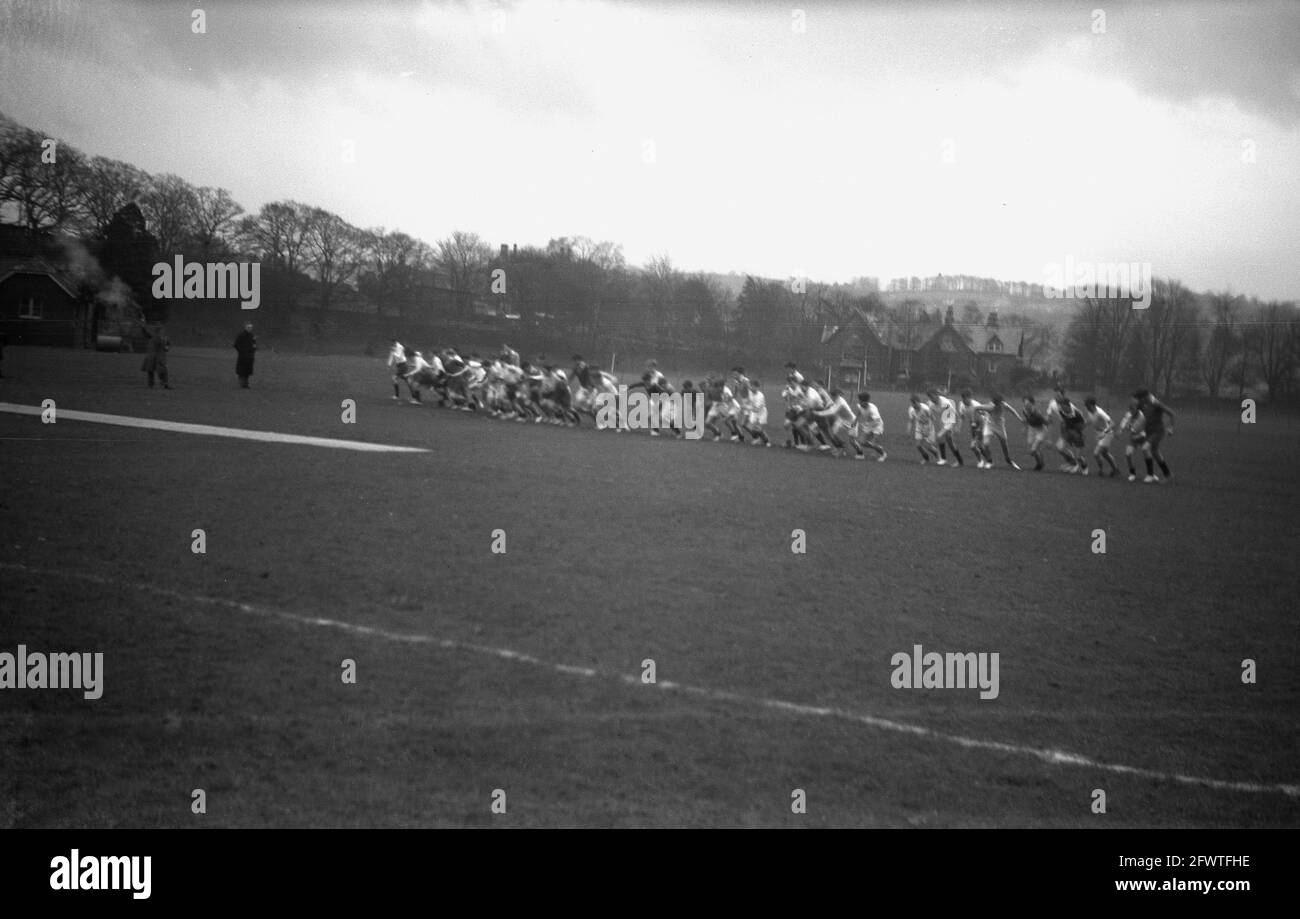 1951, storico, fuori in un grande campo sportivo, un gruppo di scolari formazione all'inizio di una corsa o di una corsa di fondo. Foto Stock