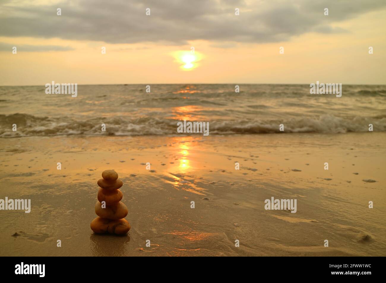 Primo piano di pietre di ciottoli equilibrate sulla spiaggia del tramonto contro gli schizzi d'onda Foto Stock