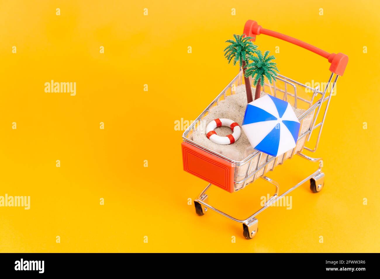 Piccolo carrello per lo shopping con sabbia, palme e accessori da spiaggia isolati in giallo. Pacchetto vacanza estate caldo concetto di prenotazione online. Foto Stock