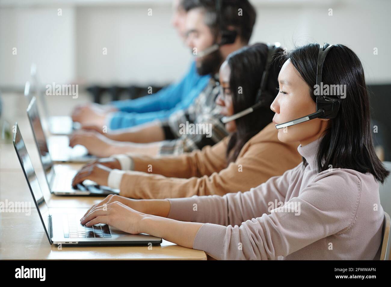 I giovani operatori interrazziali si sono concentrati sulle cuffie con microfono seduto riga e risposta alle chiamate in arrivo nel contact center Foto Stock