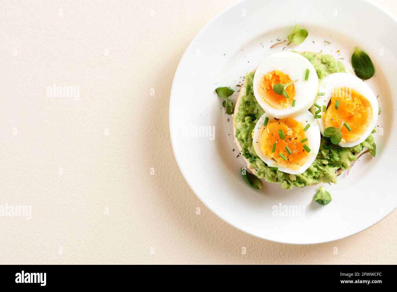 Primo piano vista del toast all'avocado con uova sul piatto su sfondo di pietra chiaro con spazio libero per il testo. Vista dall'alto, disposizione piatta Foto Stock