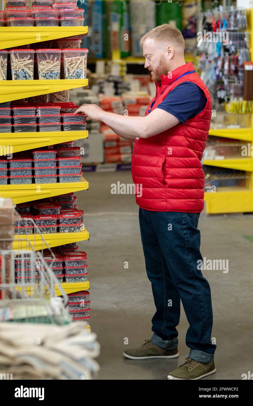 Giovane uomo che sceglie unghie nel supermercato hardware contemporaneo Foto Stock