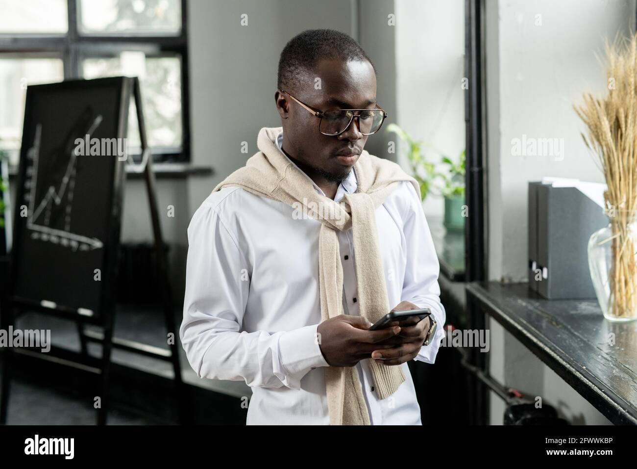 Giovane uomo d'affari di etnia africana che scorre in smartphone in ufficio Foto Stock