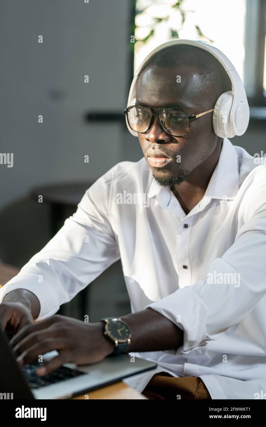Uomo serio di etnia africana che guarda l'esposizione del laptop durante l'analisi dei dati Foto Stock