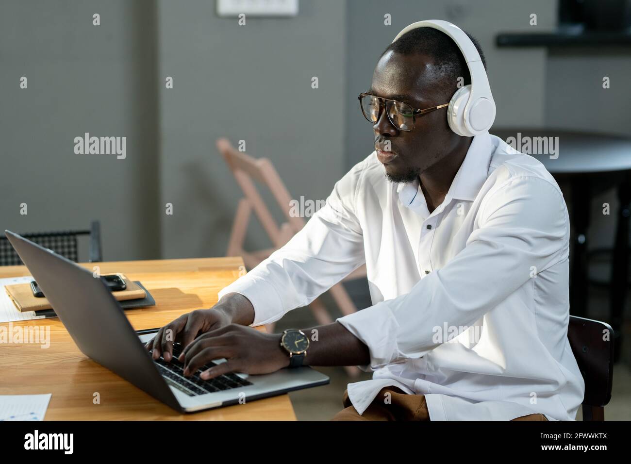 Giovane uomo d'affari di etnia africana in camicia bianca e cuffie utilizzando un computer portatile Foto Stock