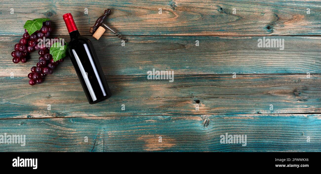 Sfondo di vino rosso con bottiglia, uva e cavatappi vintage su tavole di legno blu sbiadite Foto Stock