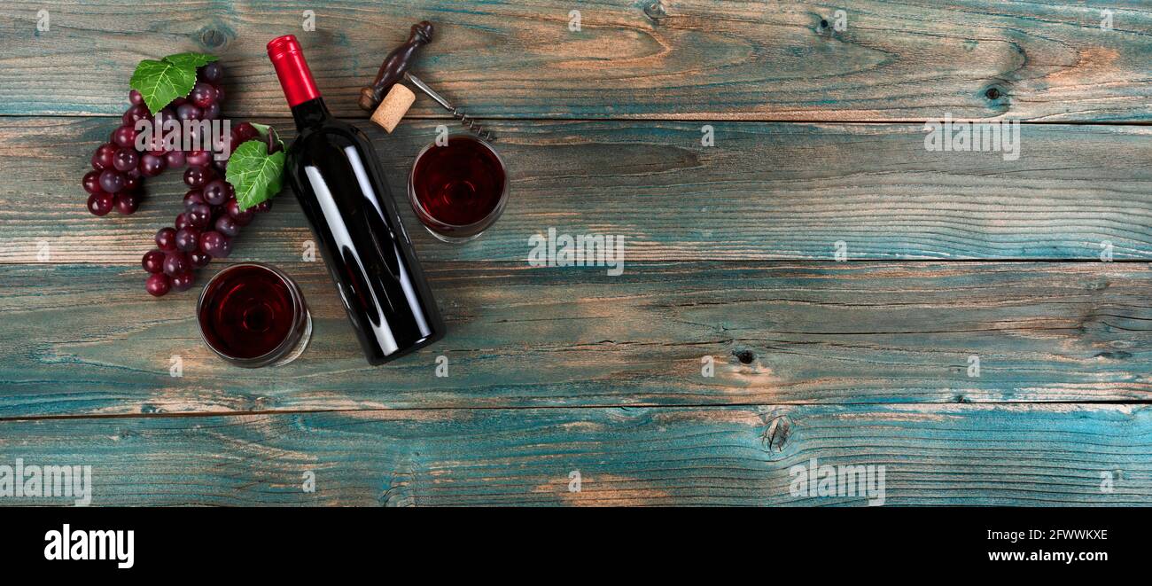 Sfondo di vino rosso con bottiglia, bicchieri da bere, uva e cavatappi vintage su tavole di legno blu sbiadite Foto Stock