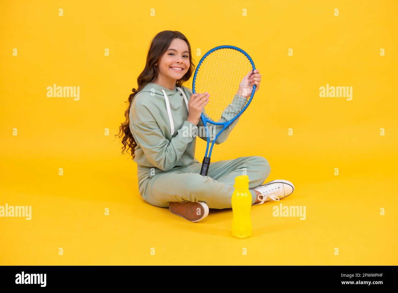 bambino sorridente seduto in abbigliamento sportivo con racchetta da squash e bottiglia d'acqua su sfondo giallo, sport Foto Stock