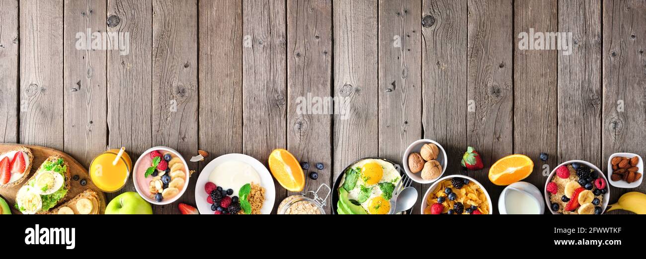 Banner cibo sano per la colazione con bordo inferiore. Tavola con frutta, yogurt, ciotola per frullati, toast nutrienti, cereali e uova. Vista dall'alto Foto Stock
