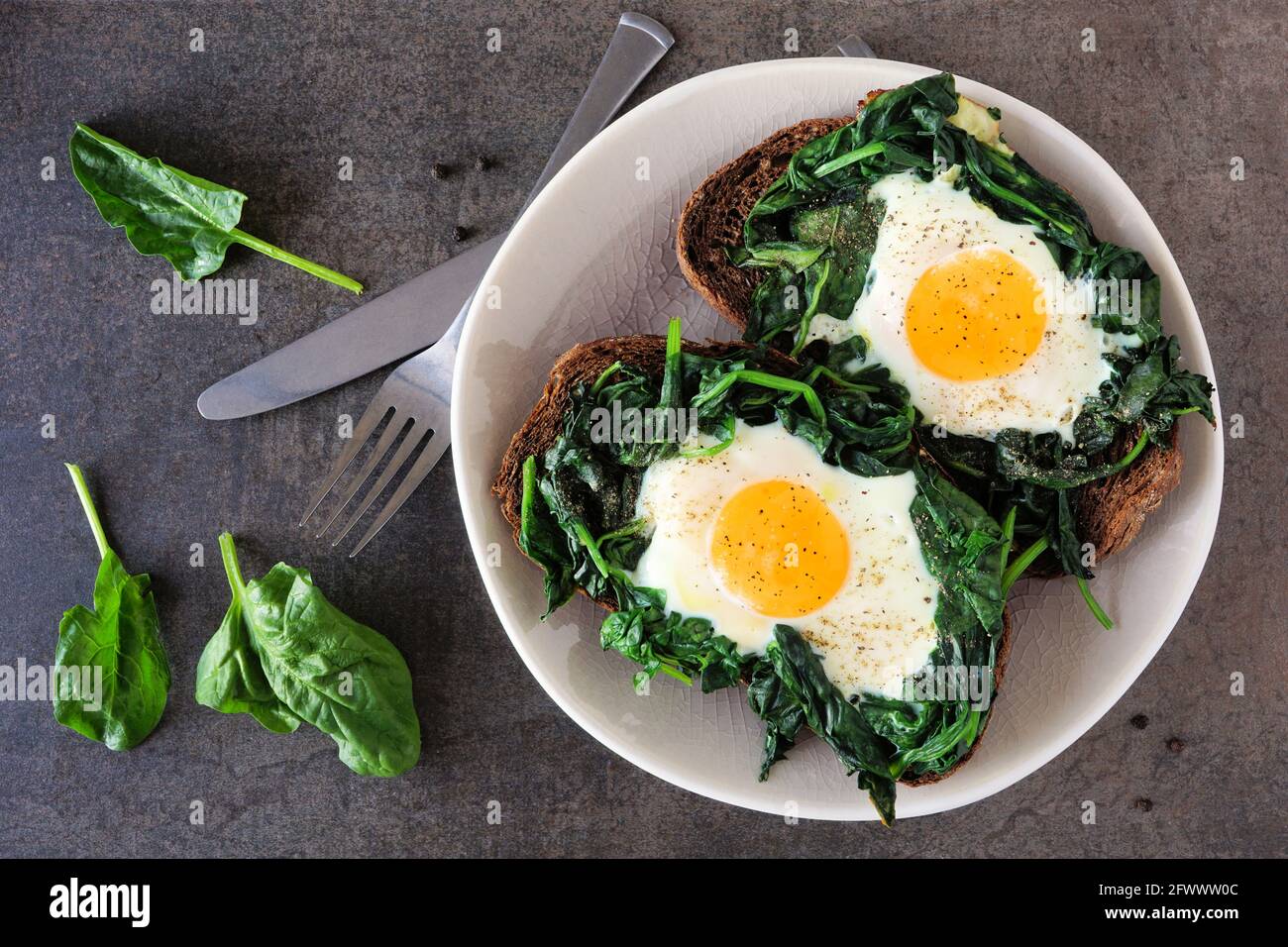 Toast sani con spinaci e uova su un piatto. Sopra la vista su uno sfondo di pietra scuro. Foto Stock