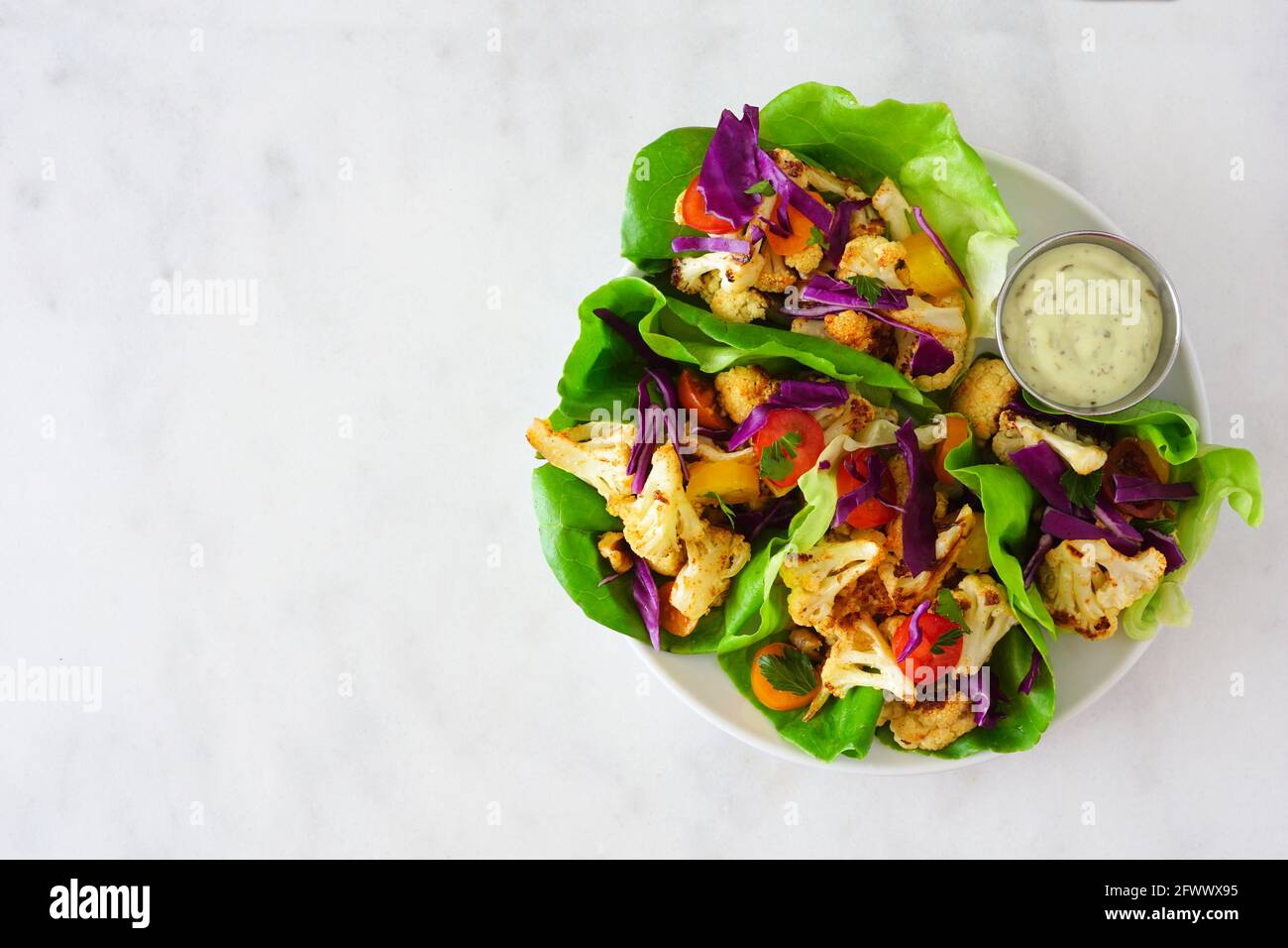 Involtini sani di lattuga con cavolfiore alla griglia, cavolo e pomodori. Vista dall'alto su uno sfondo di marmo bianco. Concetto di dieta a base di piante. Foto Stock