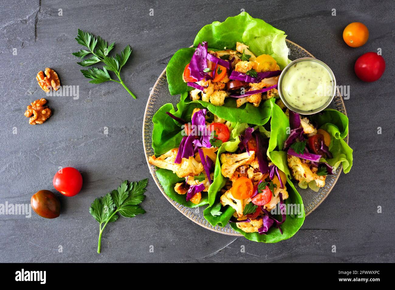 Involtini sani di lattuga con cavolfiore alla griglia, cavolo e pomodori. Vista dall'alto su uno sfondo di ardesia scuro. Concetto di dieta a base di piante. Foto Stock
