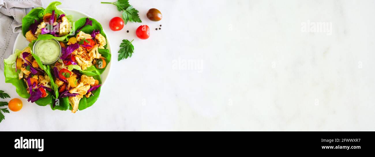 Involtini sani di lattuga con cavolfiore alla griglia, cavolo e pomodori. Bordo dell'angolo della vista dall'alto su uno sfondo di banner in marmo bianco. Dieta a base di piante c Foto Stock