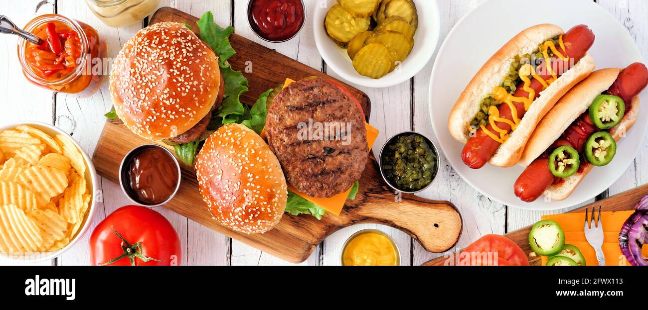 Estate BBQ scena di tavola con hot dog e buffet di hamburger. Banner con vista dall'alto su uno sfondo di legno bianco. Foto Stock