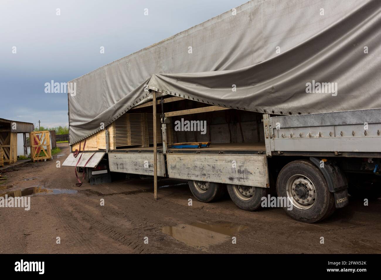 Il trattore carica tavole e legname dal magazzino dei prodotti finiti nel contenitore del carrello Foto Stock