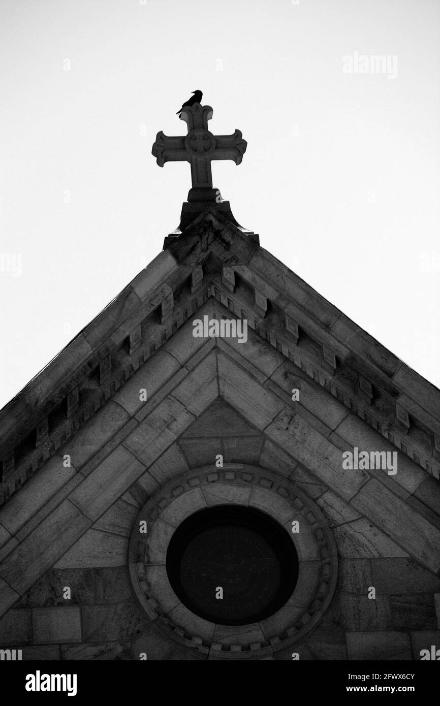 Un uccello si trova sulla cima di una croce di pietra in cima alla storica Cattedrale Basilica di San Francesco d'Assisi a Santa Fe, New Mexico. Foto Stock