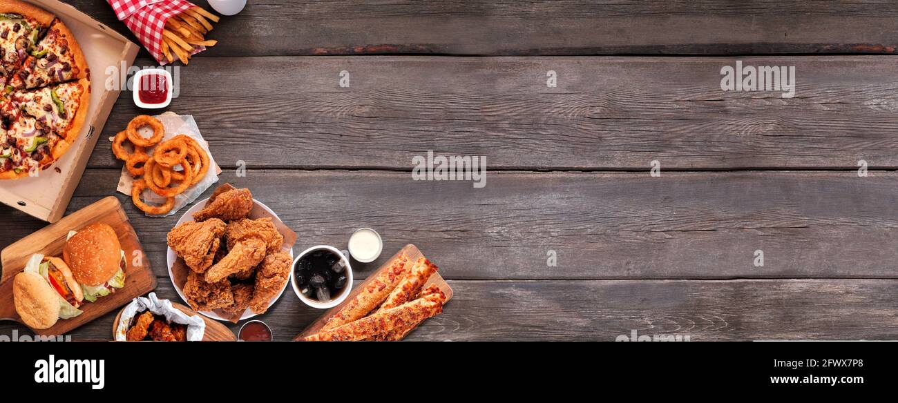 Selezione di take out e fast food. Banner bordo angolo. Pizza, hamburger, pollo fritto e contorni. Vista dall'alto su uno sfondo di legno scuro con Foto Stock